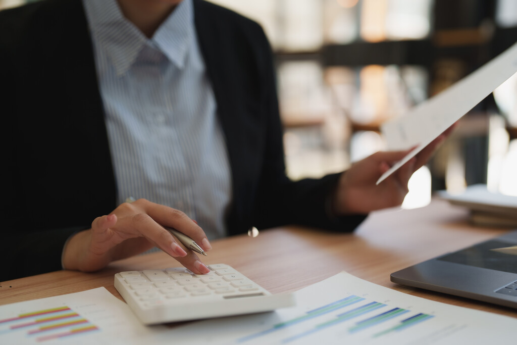 Pessoa de negócios usando calculadora e analisando gráficos de desempenho, representando o cálculo do custo total de propriedade (TCO) na gestão de ciclo de vida de ativos.
